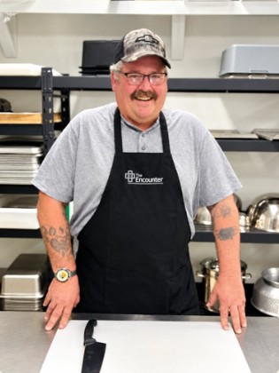 Kyle smiling in The Encounter's kitchen wearing an Encounter apron